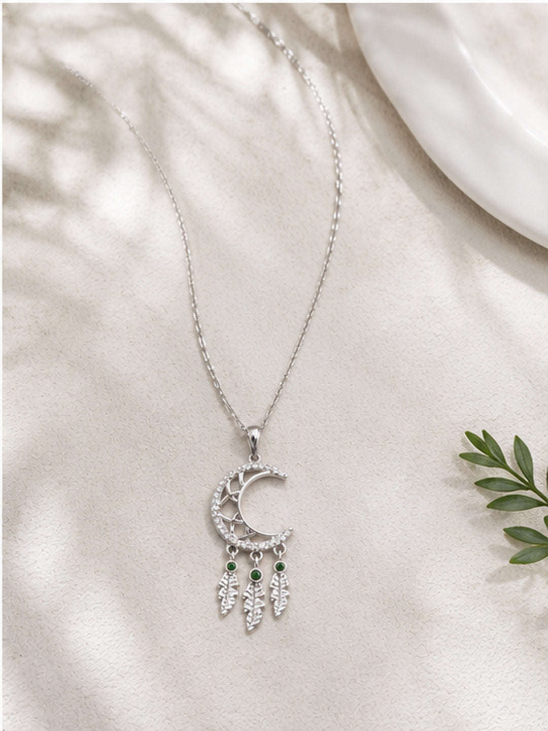 Crescent moon dreamcatcher necklace on white fabric with green leaves